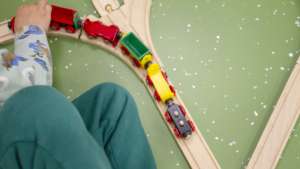 Kuvassa on lasten puinen junarata. Kuvassa näkyy myös lapsen hahmo leikkimässä.