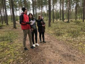 Matti, Tytti ja Nina Rajainmäki seisovat kangasmetsässä tutkimassa tulevan golfkentän aluetta. 