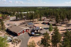Pitkäjärven vapaa-aikakeskuksen punainen päärakennus ja muita alueen rakennuksia kuvattuna ilmasta käsin aurinkoisena päivänä. 