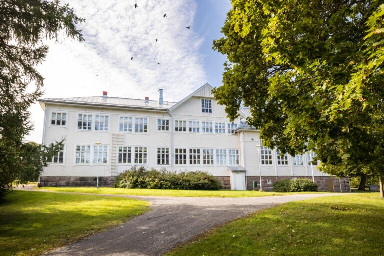 Valkoinen todella iso puinen rakennus, jossa on moniruutuisia ikkunoita.
