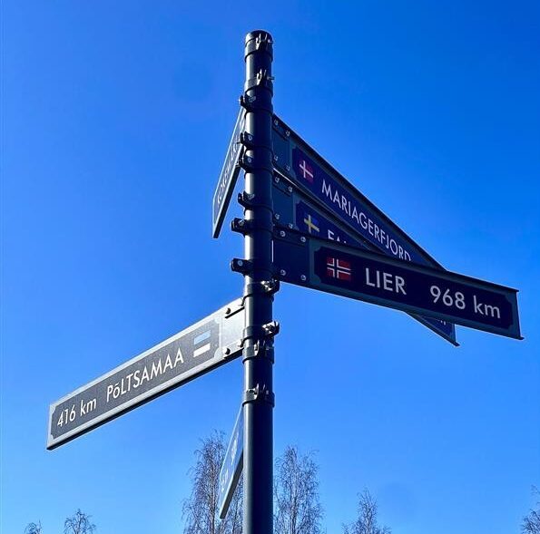 Kuvassa on kyltti lukion pihalta, jossa lukee etäisyyksiä kilometreinä Kokemäen ystävyyskaupunkeihin Euroopassa.