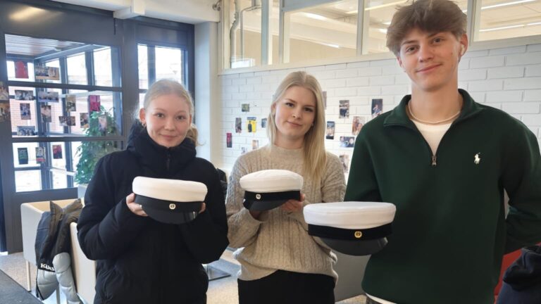 Kuvassa on kolme abiturienttia ylioppilaslakit kädessään