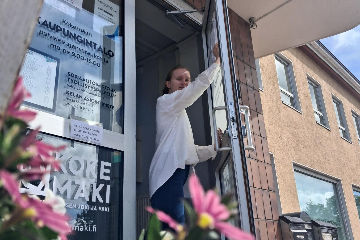 Kaupungin talo alaviistosta. Lasiiovea pitää auki harjoittelija, joka kiinnittää paperilappua kaupungintalon oveen.