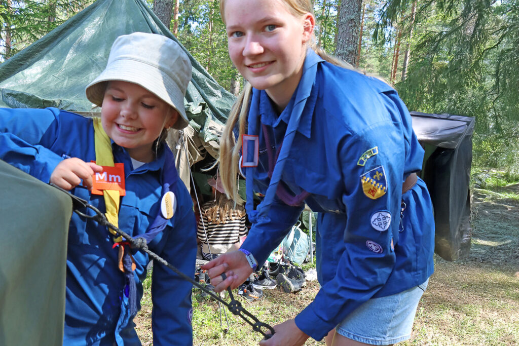 Kaksi tyttöa etualalla kiinnittävät puolijoukkuetelttaa, taustalla tyttö telassa.