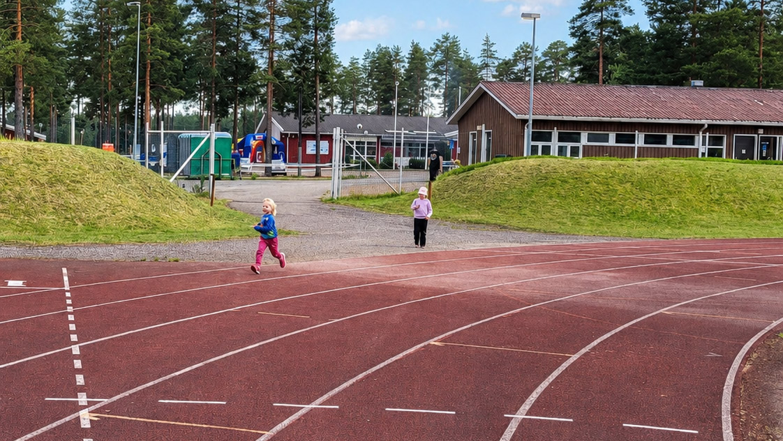 Kaksi pientä lasta juoksemassa urheilukentällä.