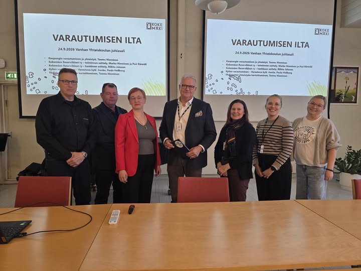 Ryhmäkuva luokan ettuosassa taustalla heijastettuna kaksi projektorikuvaa.