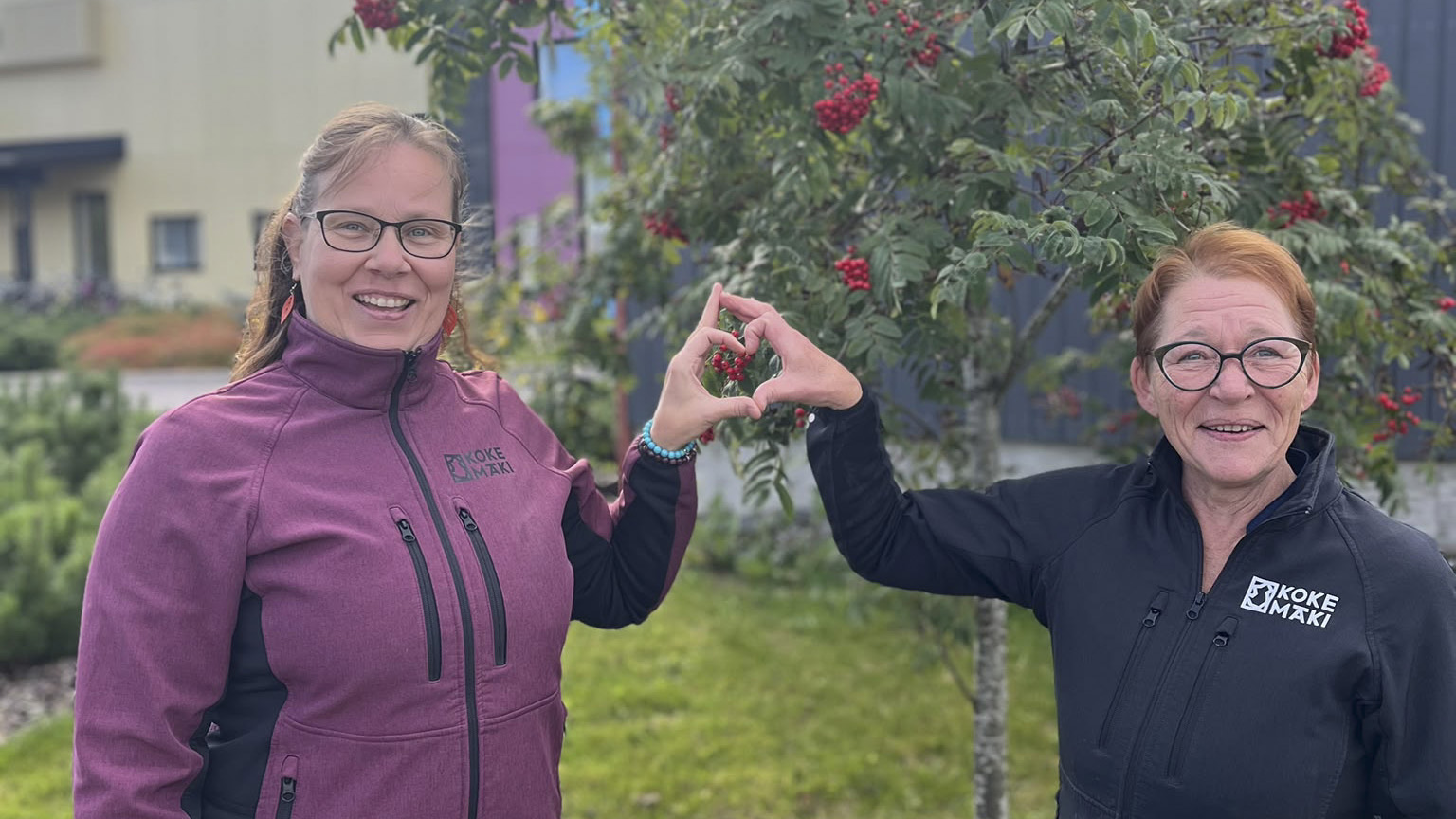 Kaksi naista iloisilla ilmeillä kädet yhdessä.
